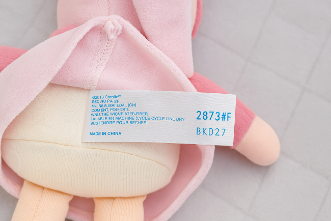 Étiquette de poupée Corolle® avec informations d’entretien et de fabrication, sur fond matelassé