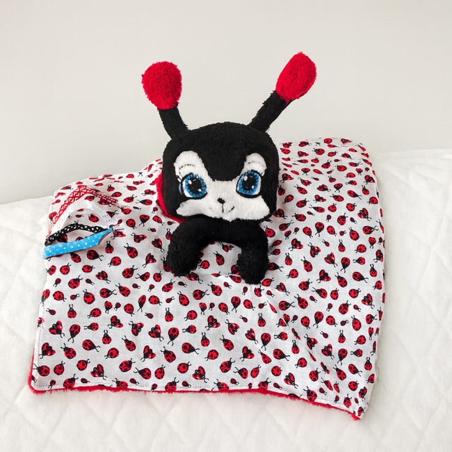 Tissu blanc à motif coccinelles avec rubans sensoriels colorés cousus sur le bord