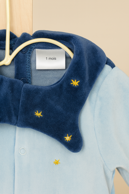 Détail du col d’un pyjama bébé bleu avec étoiles brodées et étiquette taille 1 mois