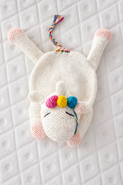 Doudou licorne en crochet blanc avec sabot rose, crinière fleurie multicolore, yeux fermés brodés