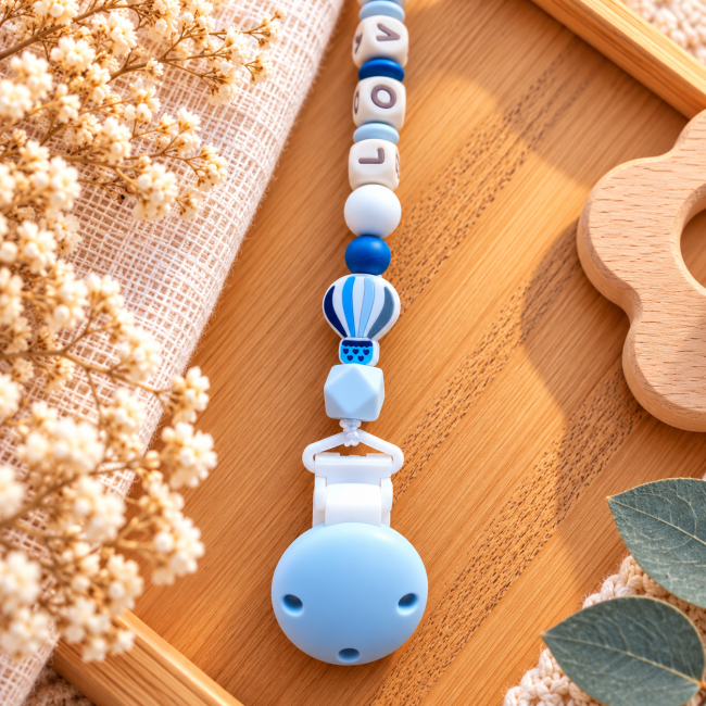 Montgolfière bleue et pince blanche Gros plan sur la montgolfière en silicone bleu et blanc, la perle géométrique et la pince blanche de l’attache sucette
