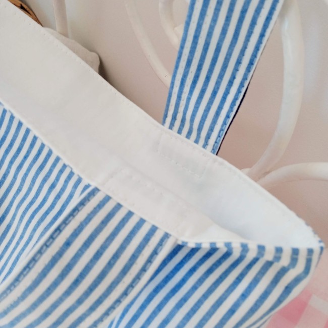 Détail des anses et de la finition d'un petit sac de messe en tissu rayé