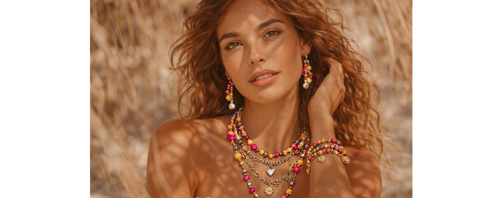 Femme bohème chic portant un assortiment de bijoux colorés Caprissa avec collier, boucles d’oreilles et bracelet en acier inoxydable, tons rose fuchsia, jaune et marron.