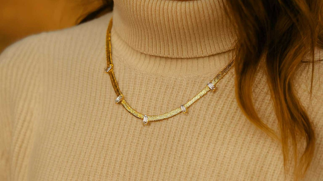 Collier doré à maille serpent orné de zirconiums blancs, bijou élégant Caprissa Créations sur pull beige à la lumière naturelle