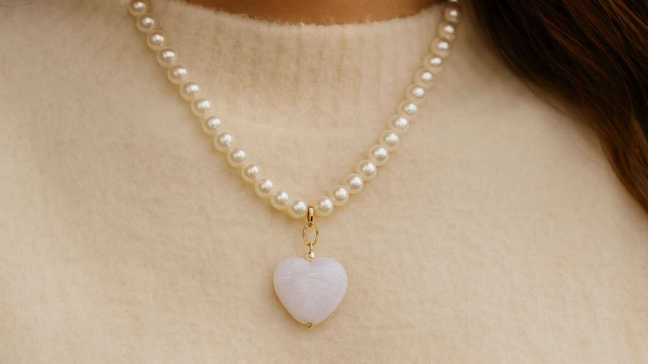 Collier San Valentino en perles nacrées avec pendentif cœur, porté sur un pull crème — bijou doré élégant et féminin signé Caprissa Créations.