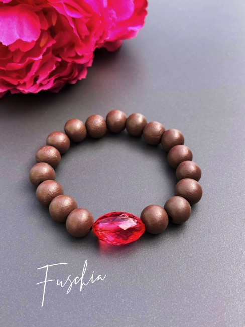 Bracelet fantaisie composé de perles de bois d'un brun mat et d'une perle de verre ovale à la couleur éclatante rose fuschia pour un contraste à la fois chaleureux et lumineux.