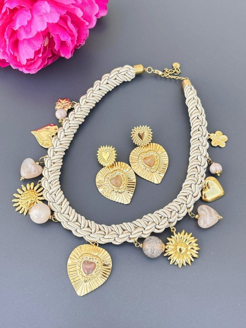 Collier chic au style italien formé par un cordon tressé beige miel et réhaussé par des pampilles en acier inoxydable doré en forme de coeur de soleil et de fleur avec des perles de résine