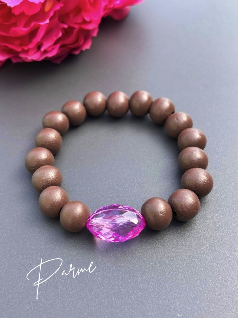 Bracelet fantaisie composé de perles de bois d'un brun mat et d'une perle de verre ovale à la couleur éclatante parme pour un contraste à la fois chaleureux et lumineux.