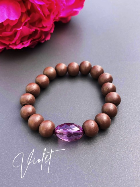 Bracelet fantaisie composé de perles de bois d'un brun mat et d'une perle de verre ovale à la couleur éclatante violet pour un contraste à la fois chaleureux et lumineux.