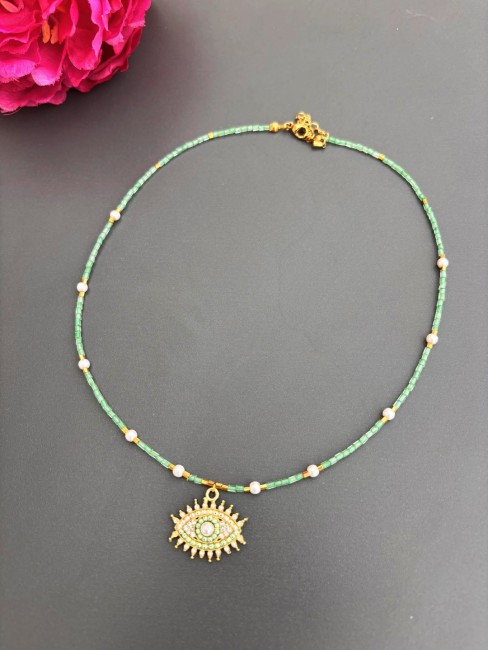 Collier fantaisie composé de perles de rocaille et d'acier inoxydable doré en forme de cube et réhaussé par un pendentif en forme d'oeil composé de strass et de perles d'eau douce. un Rendu chic solaire et bohème  pour ce collier porte bonheur