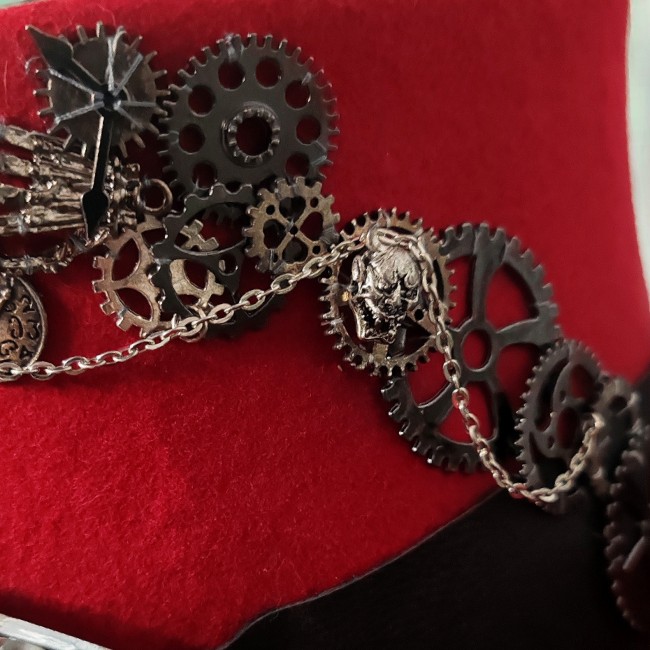 Zoom sur engrenages, chaînettes et crâne démon en métal argenté cousus sur le chapeau steampunk Dr Jekyll