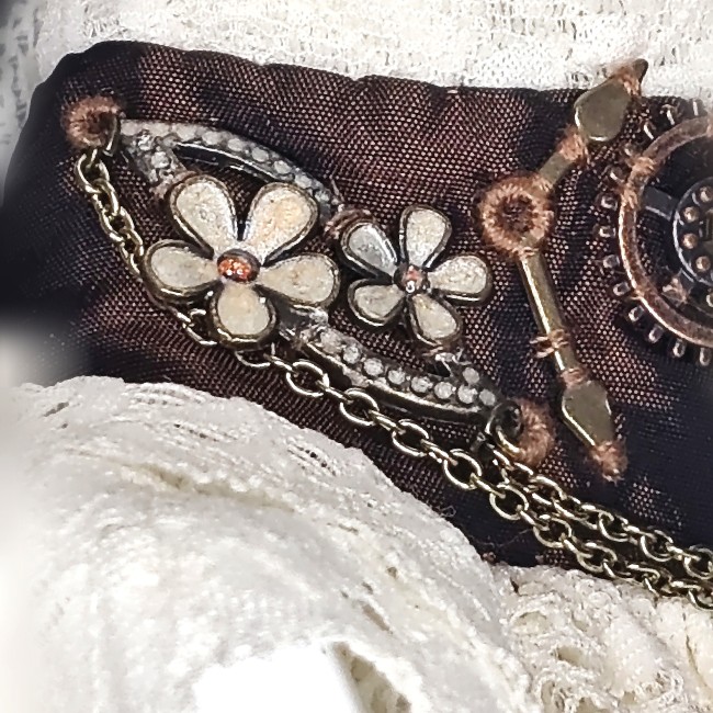 Zoom sur le côté droit du collier Cassandre, pièces florales en laiton émaillé ivoire et cuivre, éléments d’horlogerie et chaînettes brodées