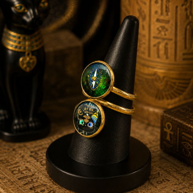 Vue de profil trois quarts de la bague L’Émeraude des Deux Rives, avec ses deux cabochons émaillés à la main, présentée sur un support noir dans une atmosphère inspirée de l’Égypte ancienne.