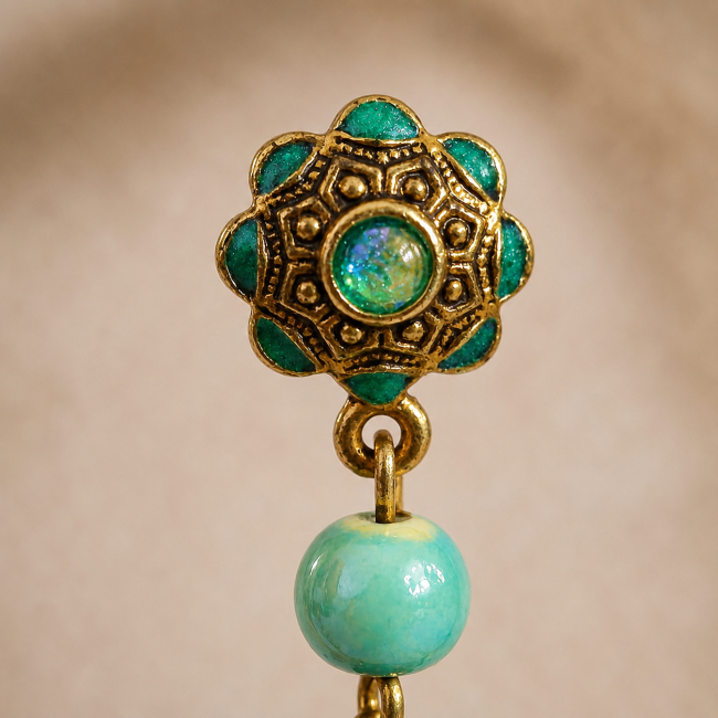 Gros plan sur le clou d'oreille ciselé et émaillé à la main dans un turquoise scintillant, accompagné de sa perle en céramique.
