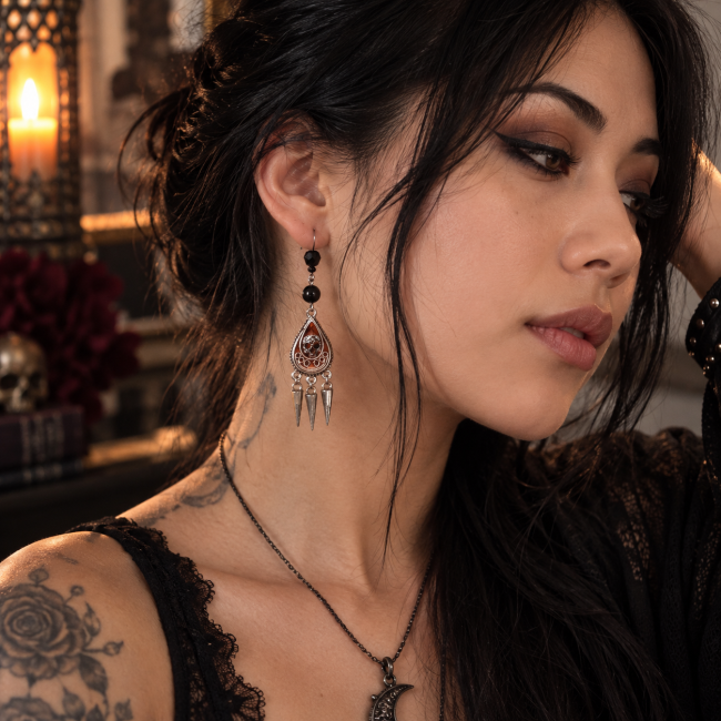 L’Épine d’Obsidienne portée – Boucles d’oreilles gothiques artisanales L’Épine d’Obsidienne portée par une femme, boucles d’oreilles gothiques artisanales avec obsidienne noire et médaillons émaillés à la main