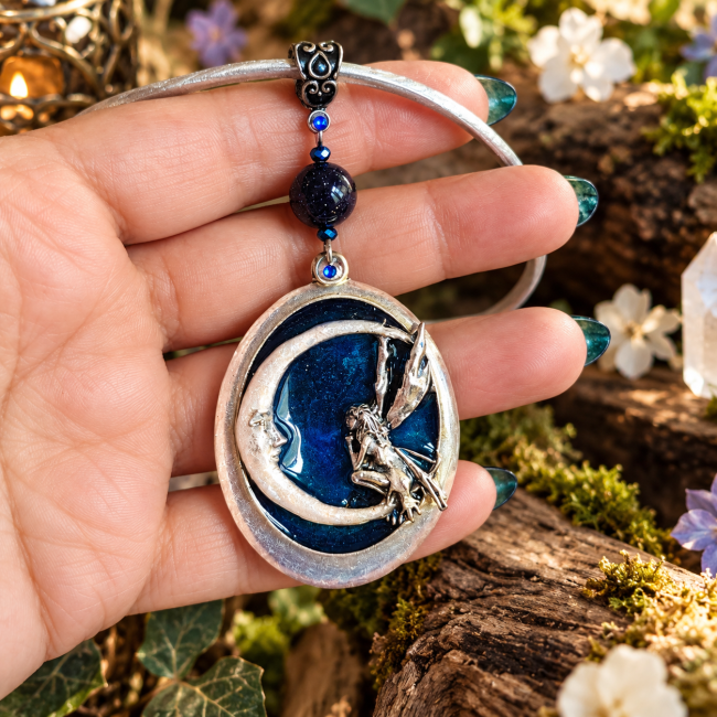 Collier artisanal Le Miroir aux Fées, avec une fée assise sur un croissant de lune en relief, émaillé de nacre transparente sur fond bleu marine scintillant, présenté dans son écrin.