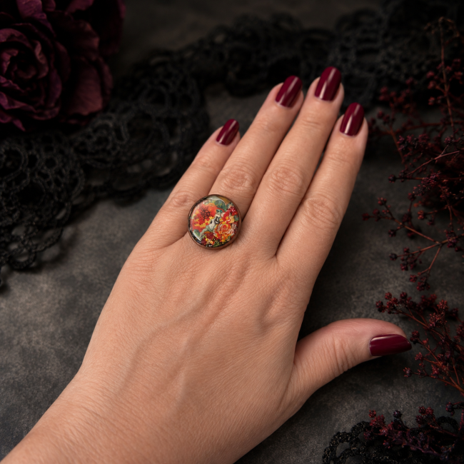 Bague Le Crâne Écarlate portée Bague Le Crâne Écarlate portée sur une main, mettant en valeur son cabochon coloré, sa monture cuivrée et son style gothique.