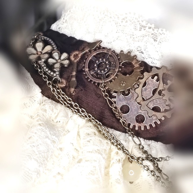 Gros plan sur les engrenages steampunk du collier Cassandre, pièces d’horlogerie et montage brodé à la main sur le bandeau