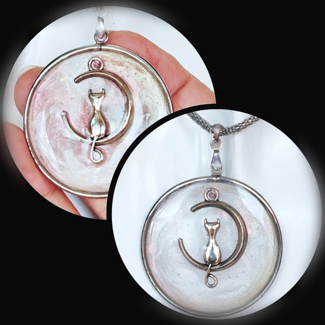  Phosphoros, un bijou entre rêve et lumière. Chaque collier met en valeur un pendentif circulaire en acier inoxydable, minutieusement émaillé à la main dans un subtil jeu de transparence rose et nacrée. Au cœur de ce pendentif, un chat délicatement posé s