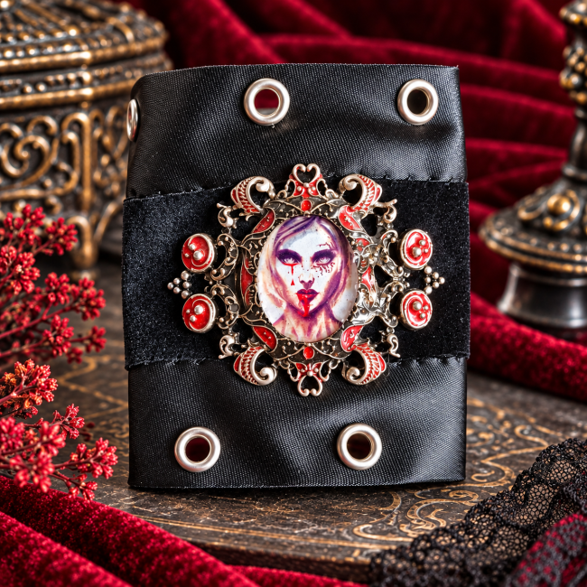 Manchette noire en satin et velours présentant un grand médaillon ornemental argenté, un portrait de vampire aux lèvres rouge sang, des motifs baroques et des rivets métalliques.