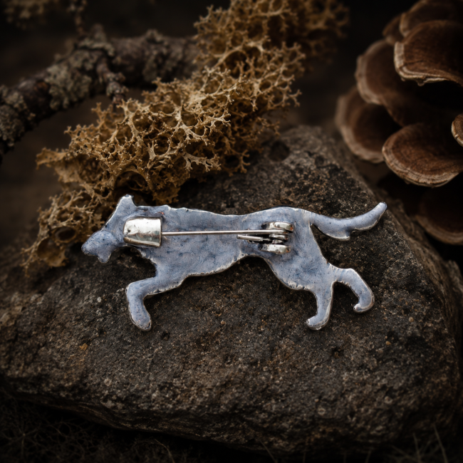 Vue arrière d’une broche artisanale argentée en forme de loup viking inspiré de Hati, avec attache métallique, posée sur une pierre dans une ambiance nordique naturelle et mystique.