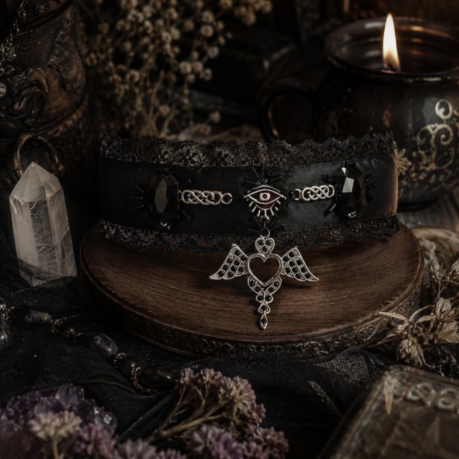 La Sybille – Tour de cou textile dans un décor mystique La Sybille mise en scène dans un décor immersif et mystérieux, mettant en valeur son satin noir, sa dentelle, ses ornements argentés et son pendentif symbolique.