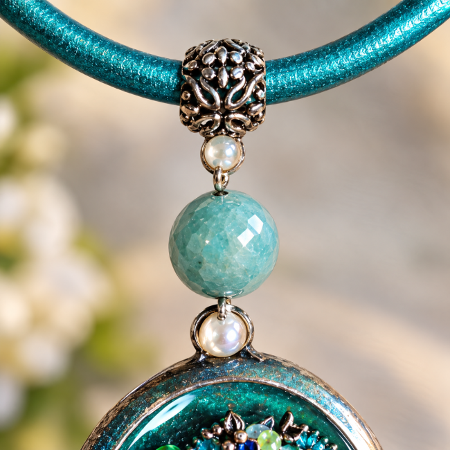 Gros plan sur la bélière ouvragée et la perle de jade turquoise reliant le pendentif au cordon du collier artisanal.
