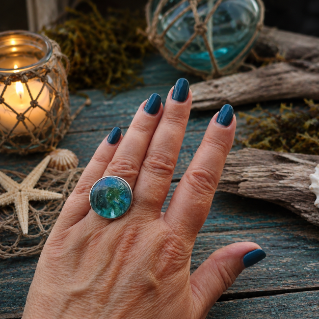bague femme 3D Le Chant des Abysses vue porté sur la main Le Chant des Abysses, bague femme réglable en acier inoxydable argenté, ornée d’un cabochon turquoise avec sirène et décor marin en relief 3D, émaillé artisanalement à la main.