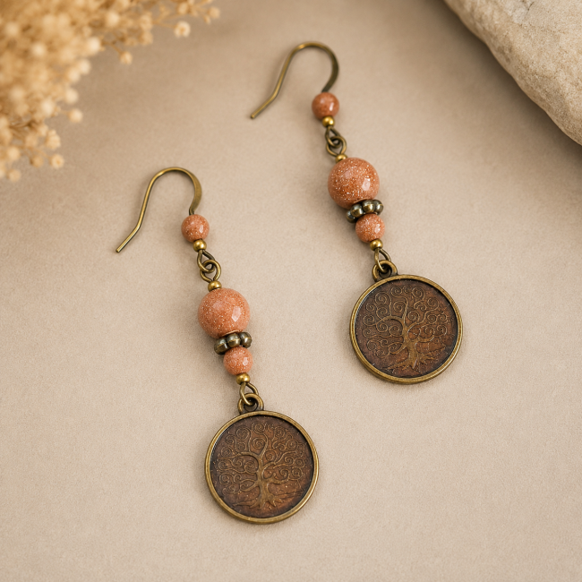 Boucles d'oreilles en pierre de soleil – Les Murmures de l'Équinoxe Vue rapprochée des boucles d'oreilles artisanales en laiton cuivré et pierres de soleil avec médaillon Arbre de Vie