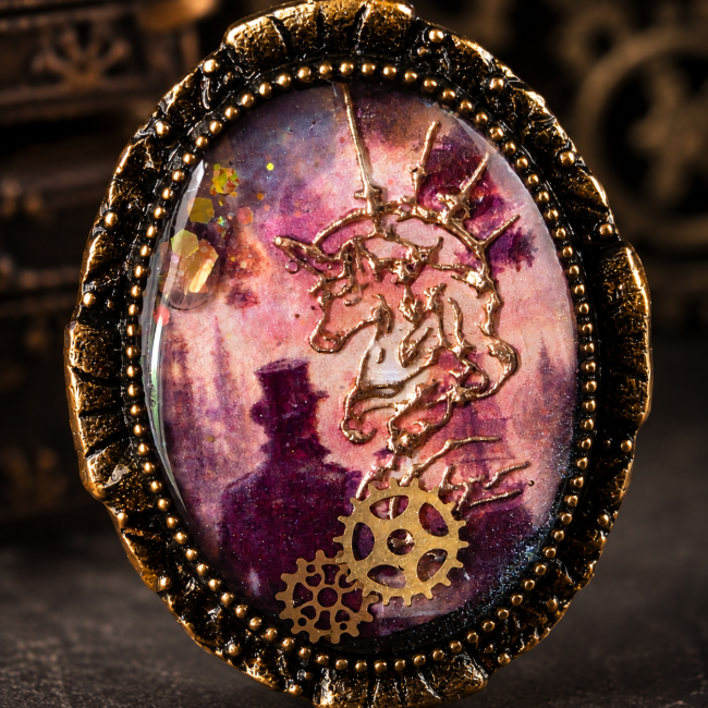 Gros plan sur le cabochon ovale émaillé à la main du Sceau du Capitaine, avec son décor de capitaine, sa caravelle, ses engrenages et sa licorne dorée.