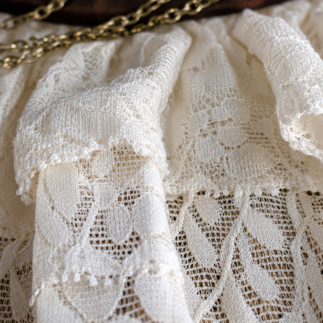 Gros plan sur la dentelle de Calais ivoire et son travail en fronces et superpositions, caractéristique de la construction haute couture du tour de cou.