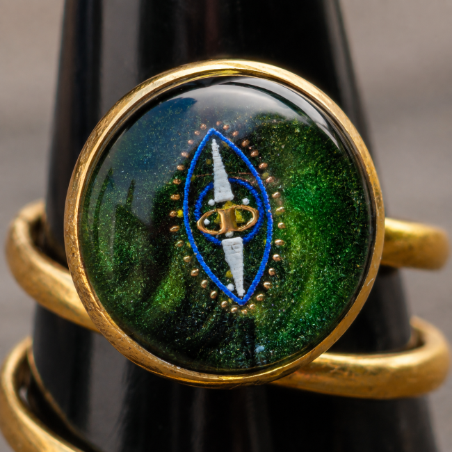 Gros plan sur le cabochon supérieur vert émeraude orné d’un motif bleu et doré de la bague L’Émeraude des Deux Rives