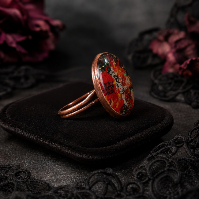 Bague Le Crâne Écarlate – Vue de profil Vue de profil de la bague Le Crâne Écarlate, mettant en valeur son cabochon bombé, sa monture en métal cuivré et son anneau réglable.