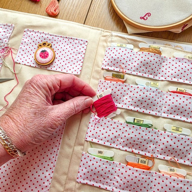 Main insérant une cartonnette de fil fuchsia dans les rangées de rangement à pois de la trousse Nina, création artisanale Angélique La Fée En Fil.