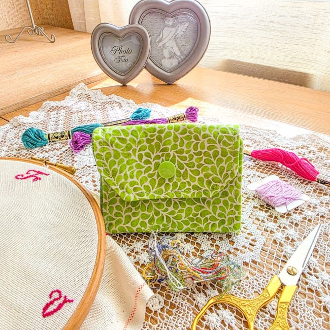 Mini poubelle à fils pliable en tissu vert anis imprimé de gouttes blanches avec bouton-pression vert, posée sur un napperon en dentelle avec accessoires de broderie, création artisanale Angélique La Fée En Fil.