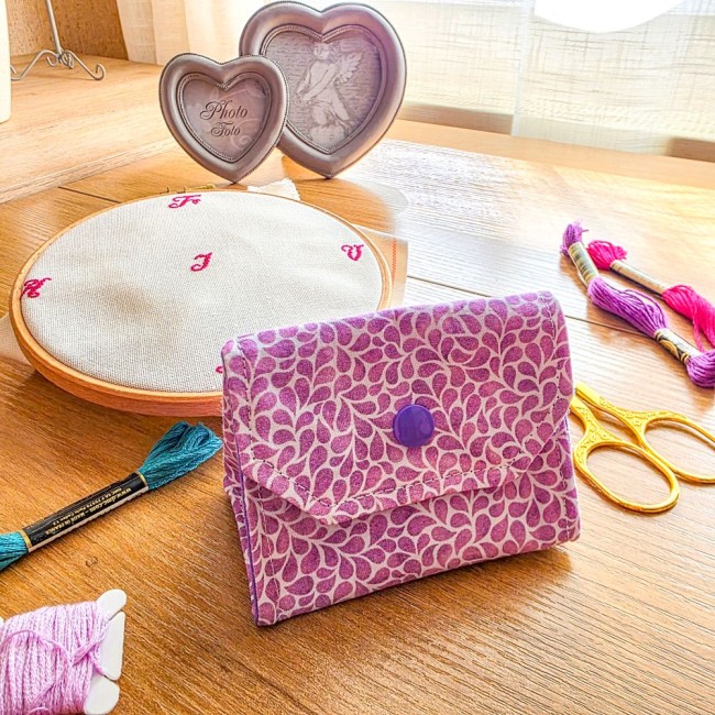 Mini poubelle à fils de table pliante modèle Lavande en tissu coton violet à motifs feuillage, fermée par bouton-pression violet, posée sur une table avec tambour à broder, ciseaux dorés et échevettes de fils, création artisanale Angélique La Fée En Fil.