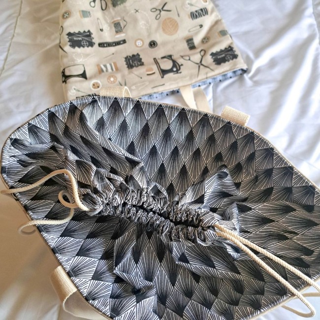 sac-cabas-fermeture-lien-coulissant-angelique-la-fee-en-fil détail sac cabas fermé par un lien coulissant posé sur un lit au loin un autre sac cabas au motif couture. Création Angélique La Fée En Fil