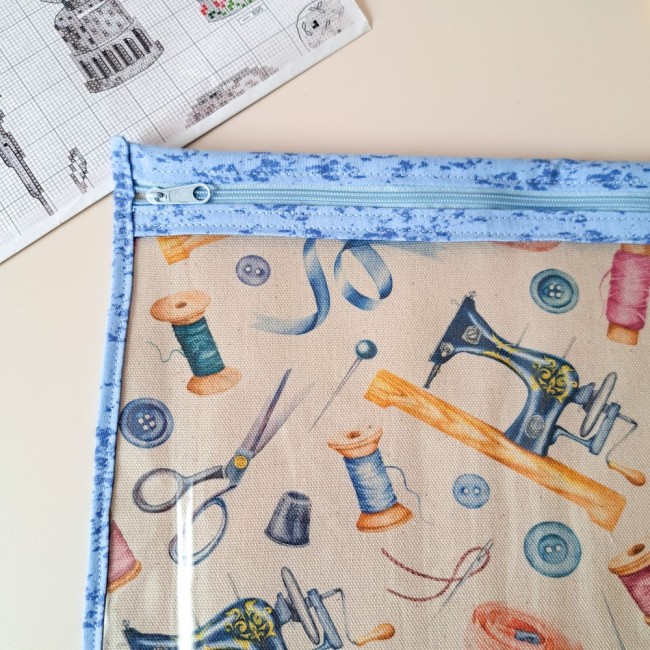 gros plan sur la pochette à projet bleu avec sa fermeture éclair assortie. tissu imprimé couture. A coté est posé une grille de point compté. Création Angélique La Fée En Fil