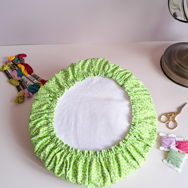 Grime Guard vert Verveine sur tambour de broderie rond, motifs végétaux, collection Lumière Végétale par Angélique la Fée En Fil. Présentation avec accessoires de mercerie.