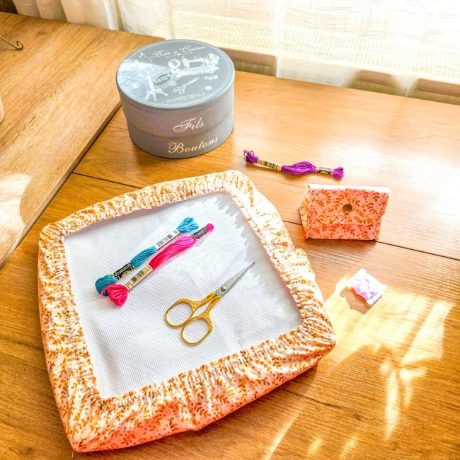Ensemble d'accessoires de broderie assortis modèle Chloé comprenant une mini poubelle à fils pliable fermée et un grime guard (housse protège-toile) pour tambour carré en tissu ocre imprimé de motifs feuillage orange et blanc, accompagnés de ciseaux dorés