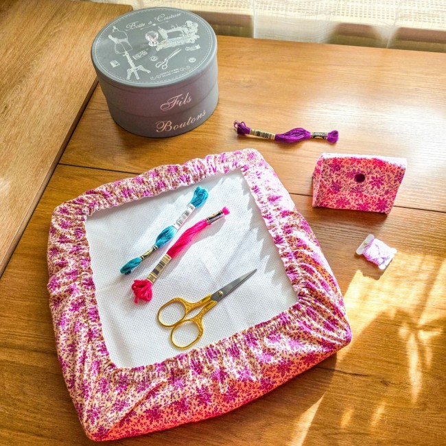 Vue d'ensemble d'un set assorti modèle Samba comprenant un grime guard housse protège-toile sur cadre et une mini poubelle à fils de table pliante en tissu coton à motifs floraux rose et violet, avec boîte de couture, ciseaux et échevettes, création artis