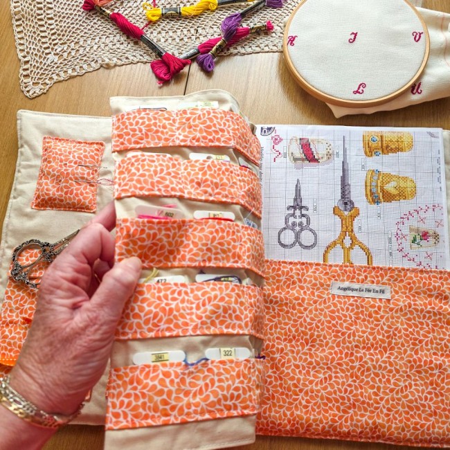 Main soulevant le rabat de rangement pour cartonnettes dans la trousse de brodeuse Savannah orange, dévoilant la grande poche avec sa grille de broderie, création artisanale Angélique La Fée En Fil.