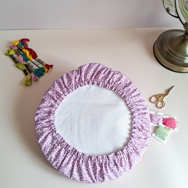 Grime Guard mauve lavande de la boutique Angélique la Fée En Fil, adapté sur un tambour de broderie rond avec toile Aïda, fils moulinés et ciseaux de précision.