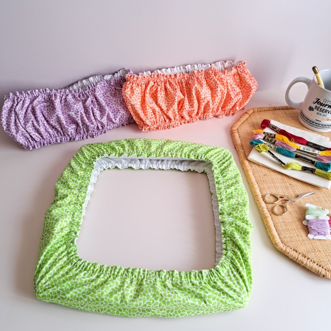 Ensemble de trois Grime Guards de la collection Lumière Végétale par Angélique la Fée En Fil : coloris vert verveine sur cadre carré, mauve lavande et orange Mandarine présentés avec une tasse et des fils à broder.