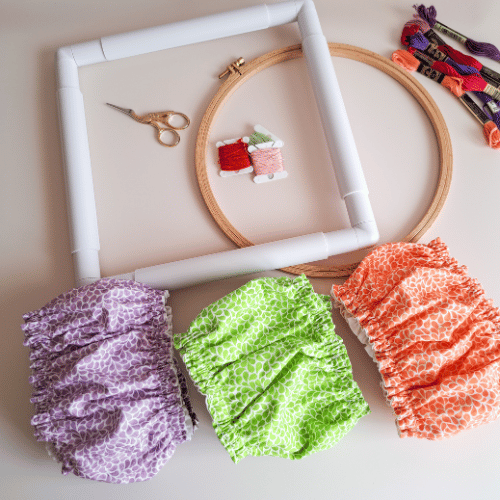 collection-lumiere-vegetale-grime-guards-lavande-verveine-mandarine-accessoires-broderie Grime guards de la collection Lumière Végétale en couleurs lavande, verveine et mandarine, présentés avec un tambour, un cadre Q-snap, des fils à broder et des ciseaux – créations artisanales Angélique La fée En Fil.