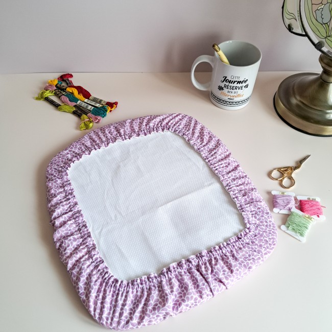 Grime Guard mauve Lavande, collection Lumière Végétale par Angélique la Fée En Fil. Protection pour cadre Q-Snap carré entourée d'accessoires de mercerie printaniers.