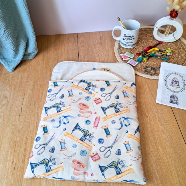 Vue de dessus d'un tambour à broder en bois glissé dans sa pochette de protection ouverte au motif couture vintage. Intérieur en tissu clair molletonné. Accessoires de broderie et mug 