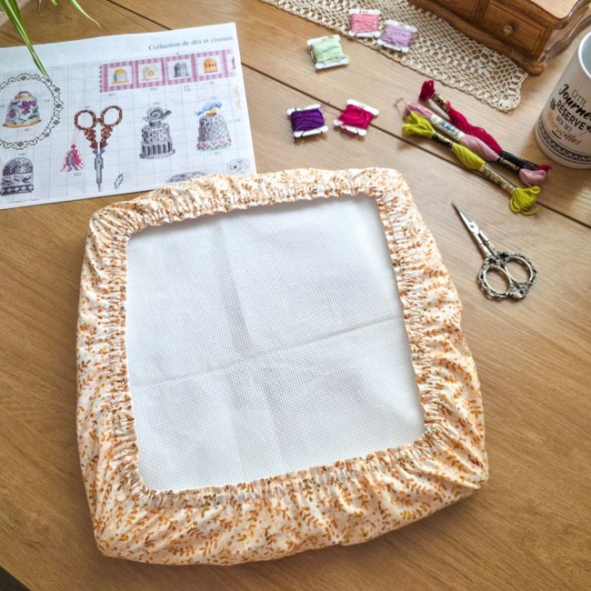 grime-guard-point-de-croix-compte-sous-bois-dore-tissu-beige-feuillage-vue-haut-qsnap-angelique-la-fee-en-fil Vue du dessus d'un grime guard modèle Sous-Bois Doré en tissu beige à motifs de feuillage ocre, ajusté sur un métier Q-Snap carré posé sur un bureau de broderie par Angélique La Fée en Fil.