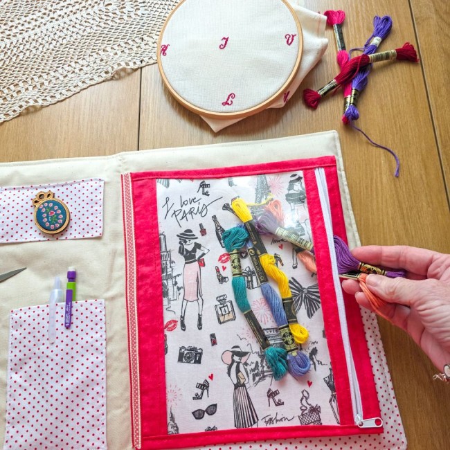 Main rangeant des écheveaux de fils dans la pochette zippée en tissu Paris de la trousse de broderie et point de croix Nina, création artisanale Angélique La Fée En Fil.