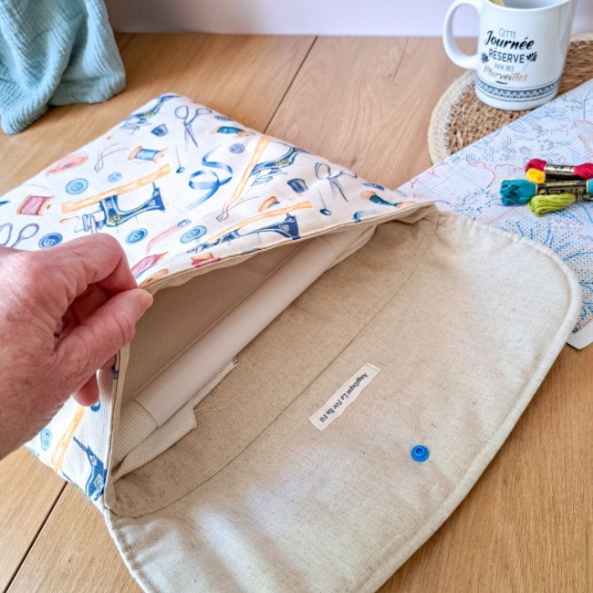 Gros plan sur l'intérieur d'une pochette à broder ouverte laissant apparaître un cadre Q-Snap. On distingue la doublure en tissu naturel, l'étiquette de la marque 